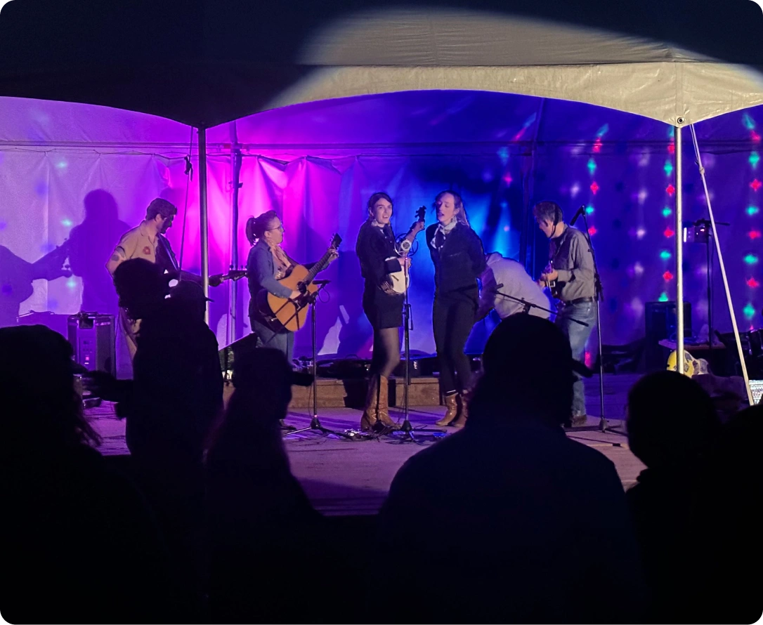 A band performs on stage under a tent with colorful stage lights