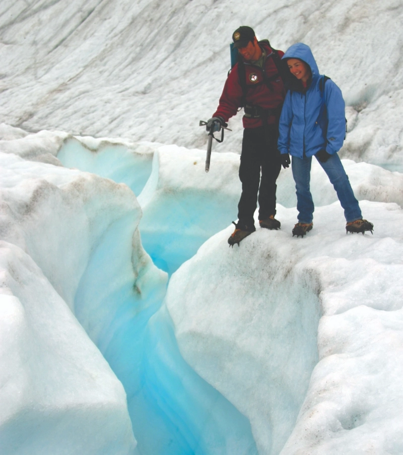 Two climbers with ice gear standing near a crevasse on a glacier