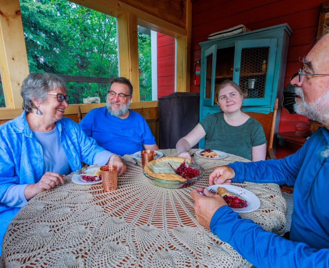 People sitting at a table with pie and copper mugs, with a nature view outside