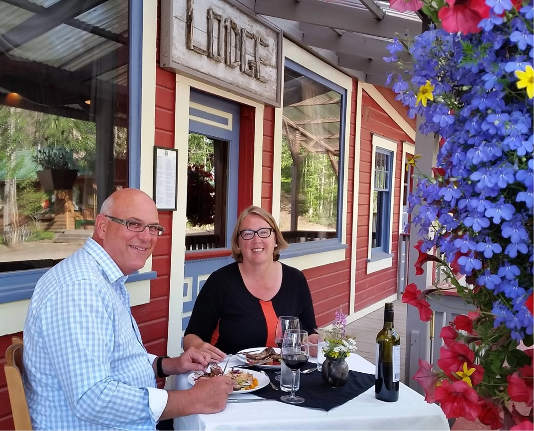 Two people dining outside a rustic building with vibrant blue and red flowers