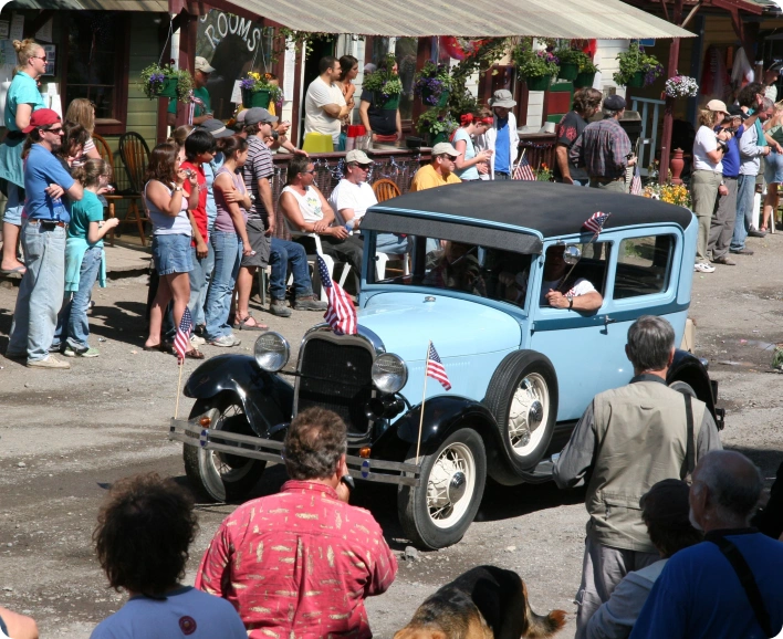 Vintage blue car at a parade, surrounded by spectators