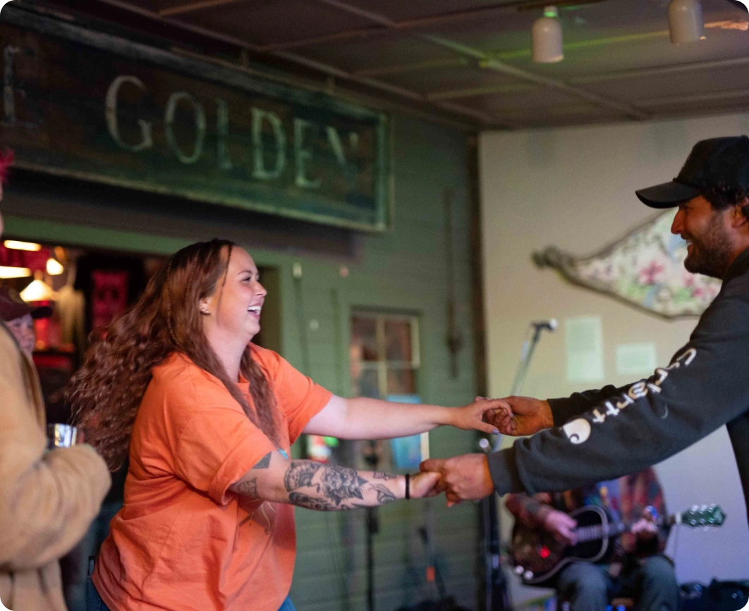 Two people dancing in a room with a musician playing guitar in the background